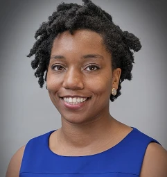 A woman with dreadlocks smiling in a blue shirt.