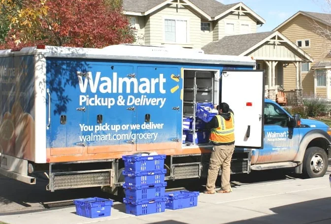 A man loading boxes into a walmart pickup and delivery truck.